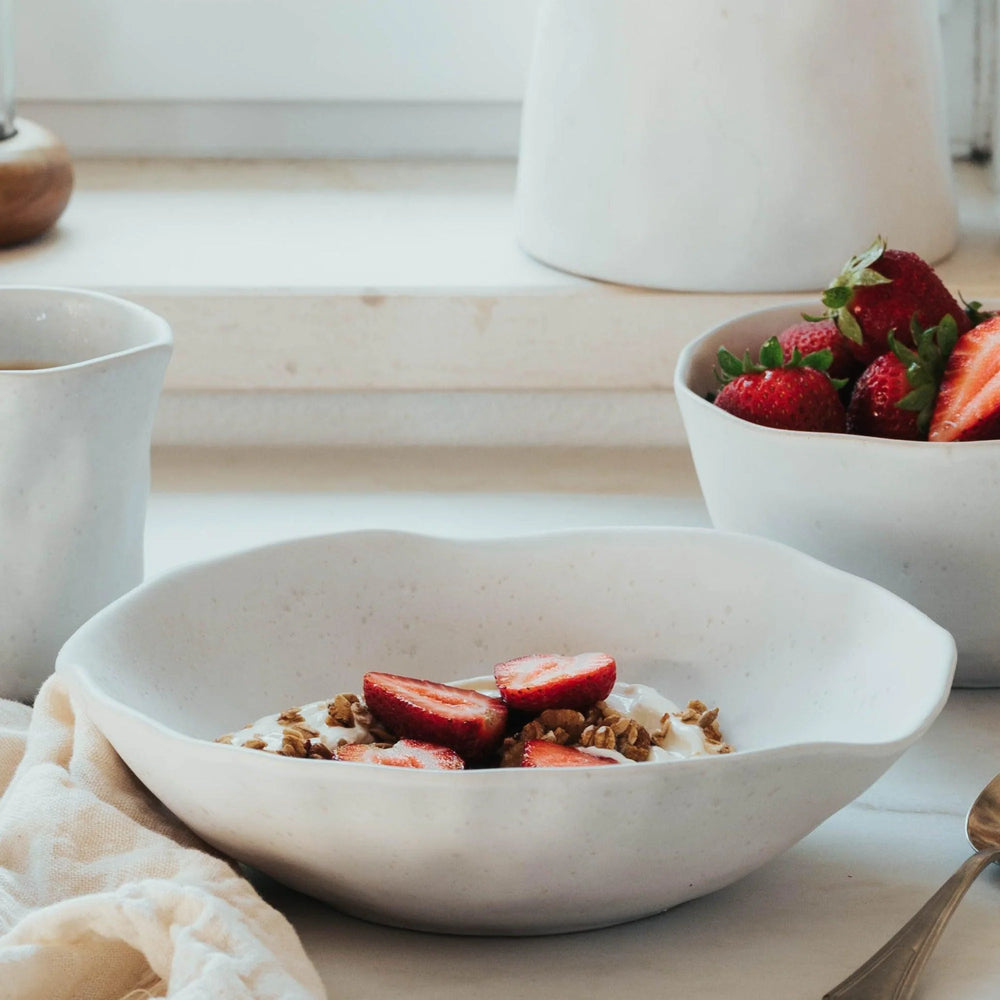 White bowl with strawberries and granola on a light wooden surface