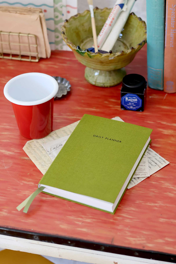 Green planner on a desk with a red cup and stationery items.