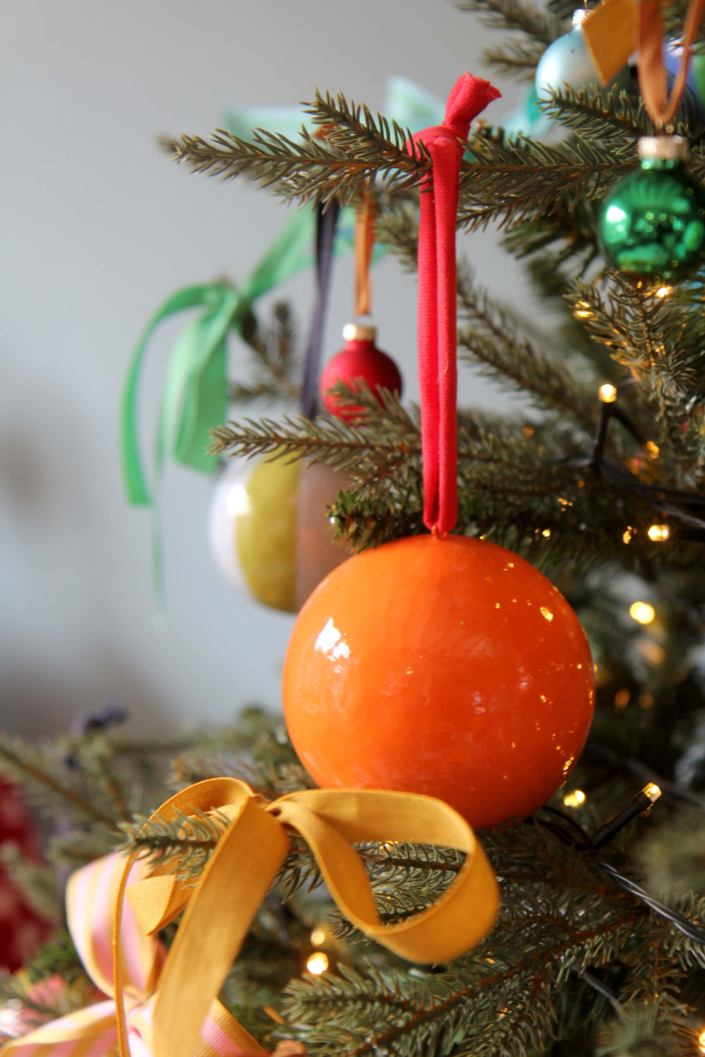 Decorative orange ball ornament on a Christmas tree with other ornaments.