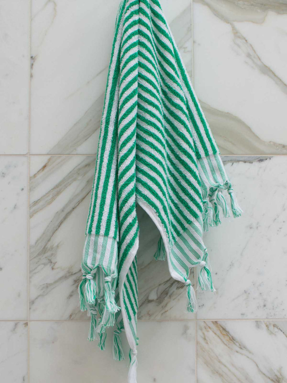 Green and white striped towel with tassels hanging on a marble wall.