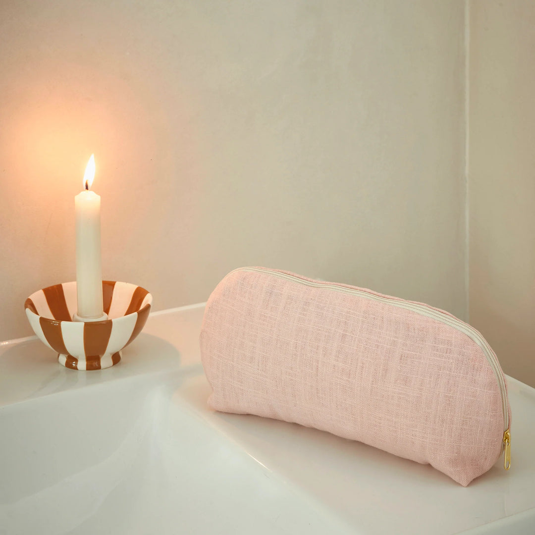 Pink make up bag on a white surface with a candle in the background