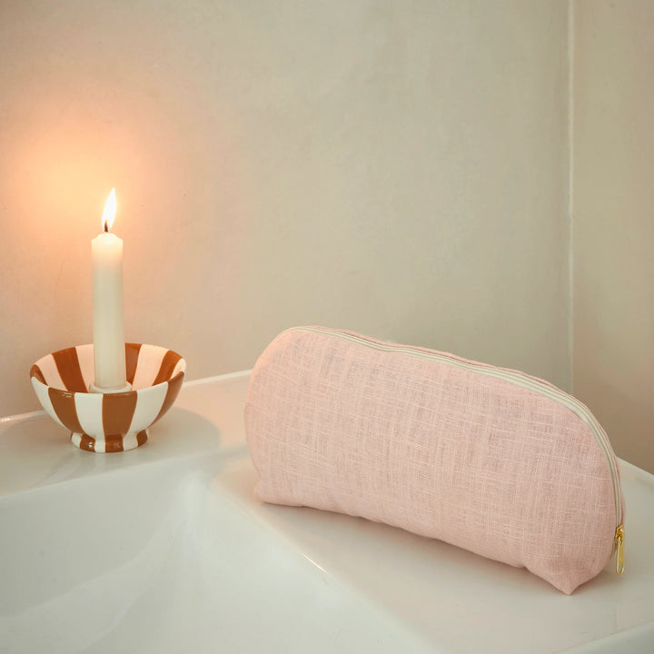 Pink make up bag on a white surface with a candle in the background