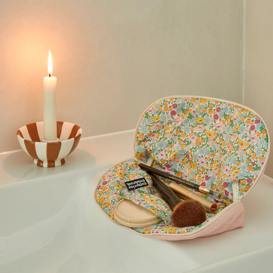 Floral makeup bag with brushes on a white surface next to a candle.