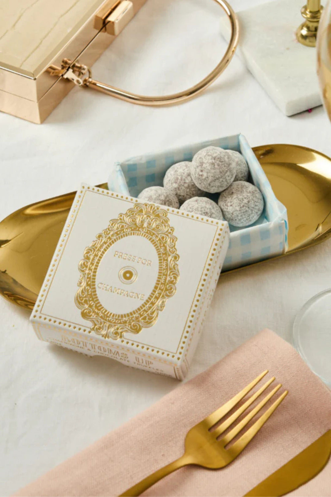 Decorative box of chocolate with gold accents on a table setting with gold cutlery and platter.