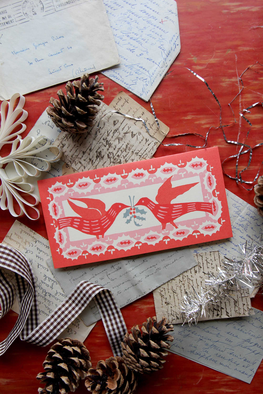 Decorative card with festive design on a red surface with pine cones and ribbons.