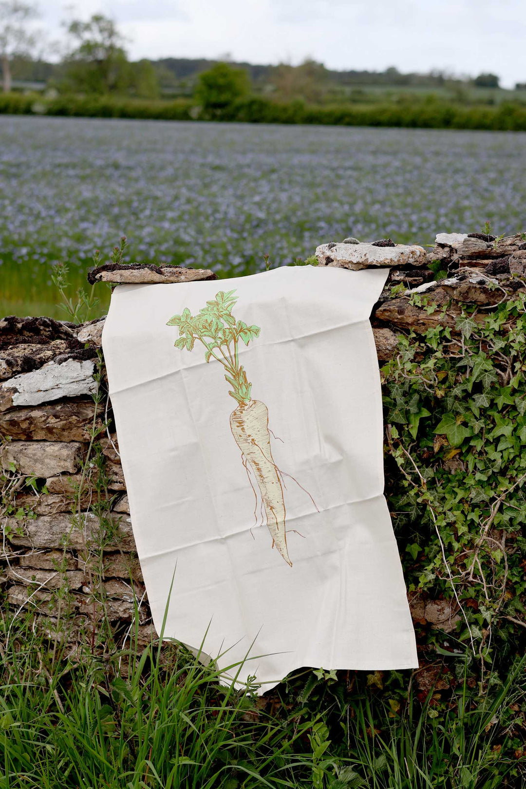 Towel with a carrot design hanging on a wooden fence by a field