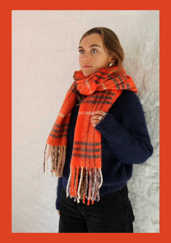 Person wearing a large orange plaid scarf against a light background