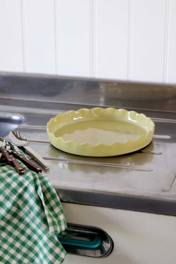 Yellow pie dish on a kitchen counter with utensils and a green checkered towel.