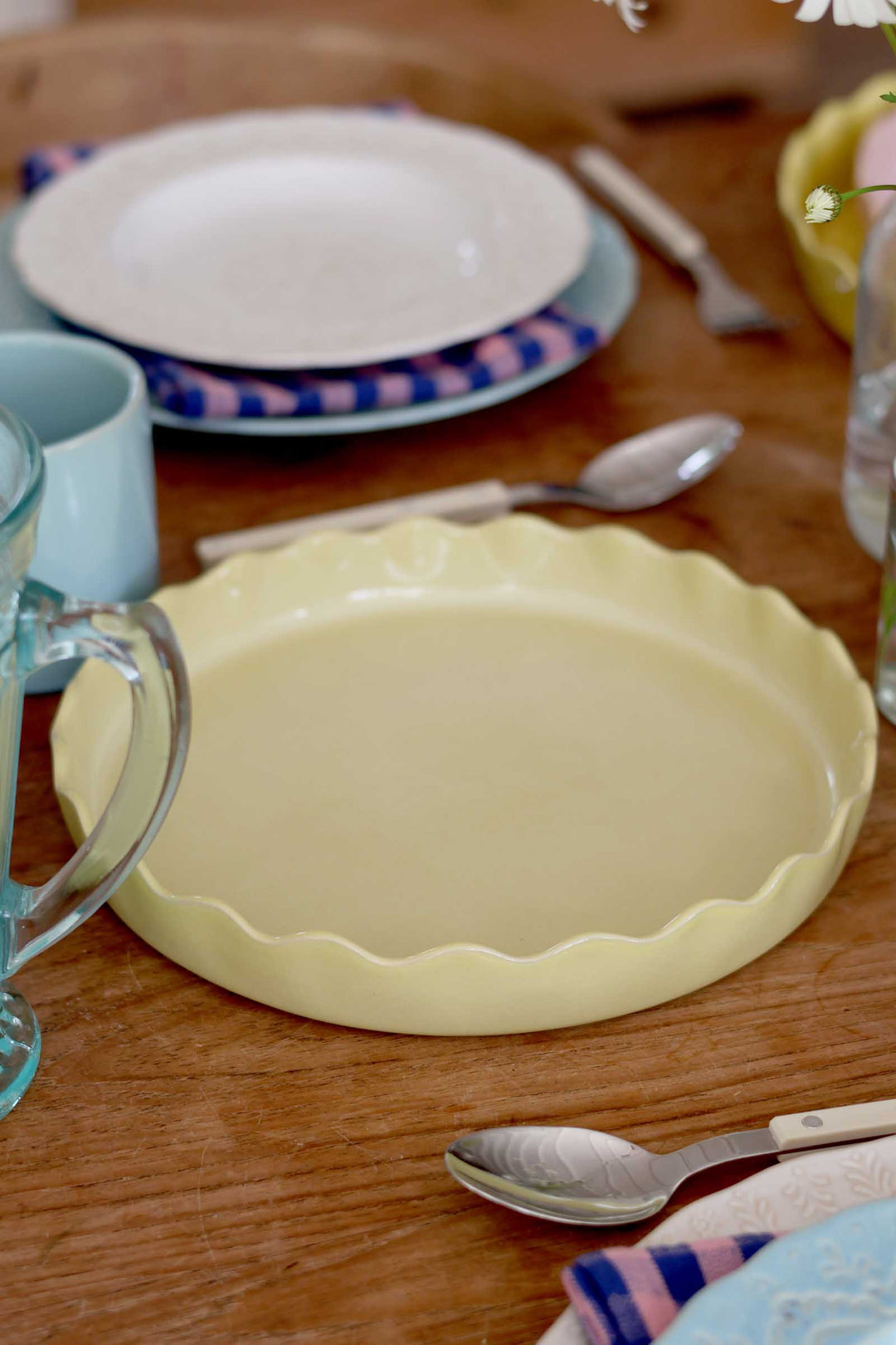 Yellow ceramic pie dish on a wooden table with plates and cutlery in the background