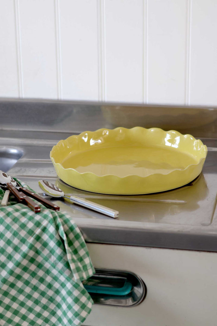 Yellow pie dish on a kitchen counter with utensils and a green checkered towel.