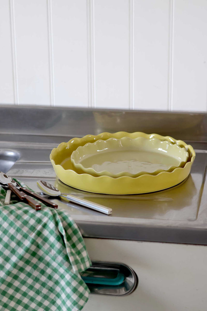 Yellow ceramic pie dish on a kitchen counter with a green checkered towel.