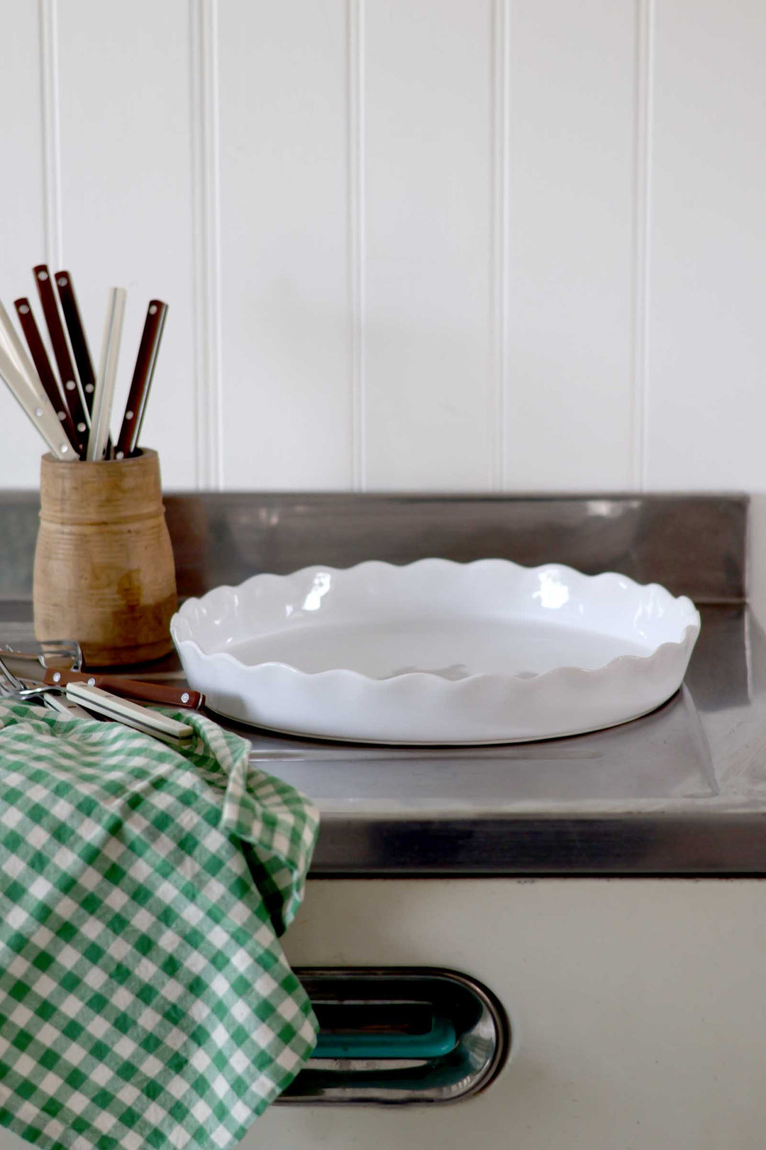 White ceramic dish on a kitchen counter with a green checkered towel and wooden utensil holder.