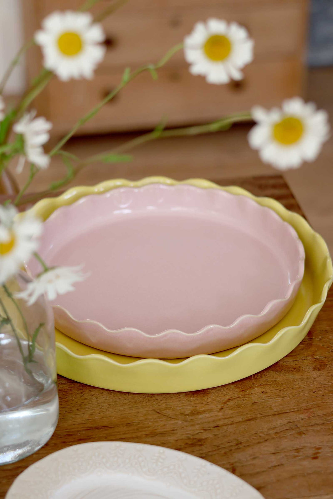 Pink ceramic plate with scalloped edge on a wooden table with daisies.