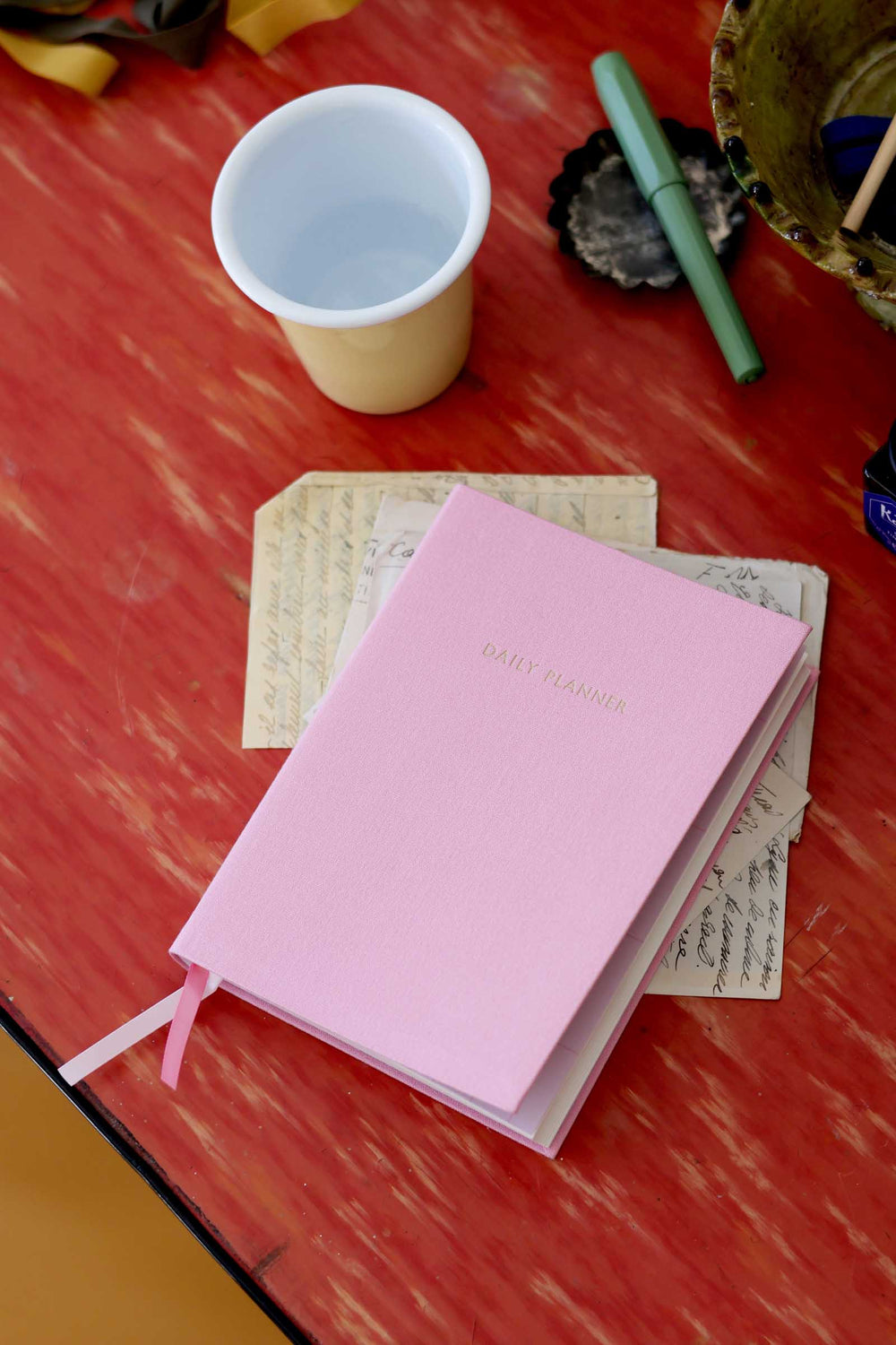 Pink notebook on a red surface with a cup and other items around