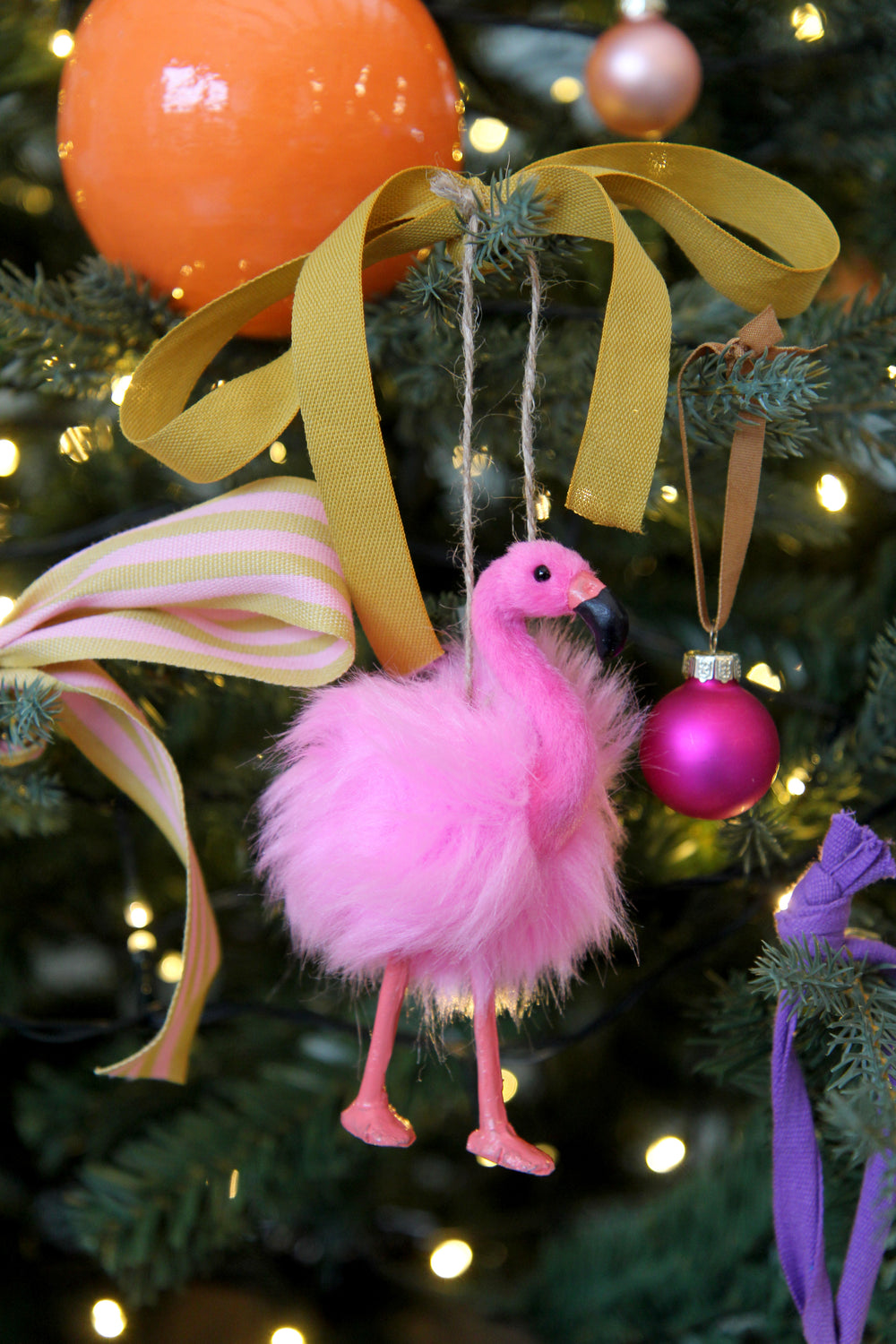Pink feathered ornament shaped like a flamingo hanging on a decorated Christmas tree.