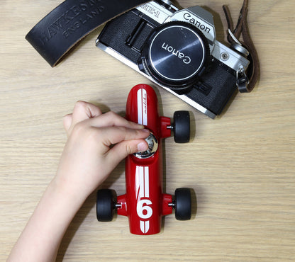 Red toy car with number 6 on a wooden surface, next to a Canon camera.