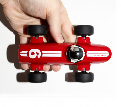 Red toy car with black wheels held by a hand on a white background