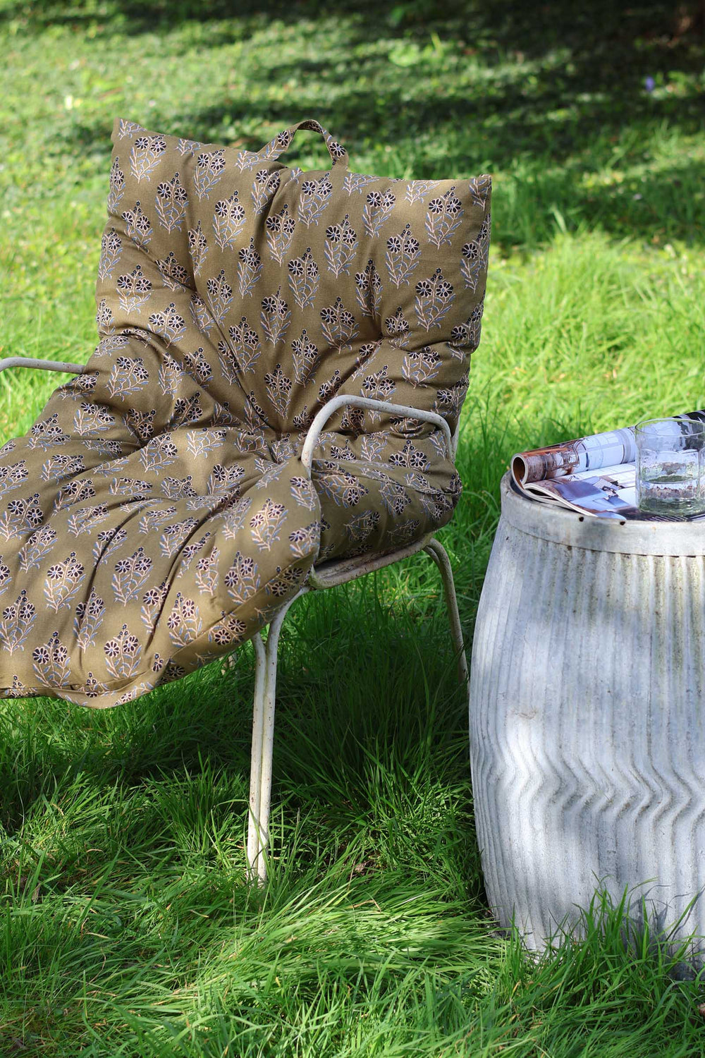 Chair with patterned cushion on grass next to a metal barrel