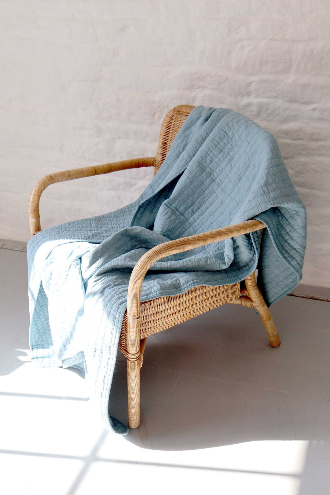 Wicker chair with a blue blanket draped over it against a light background
