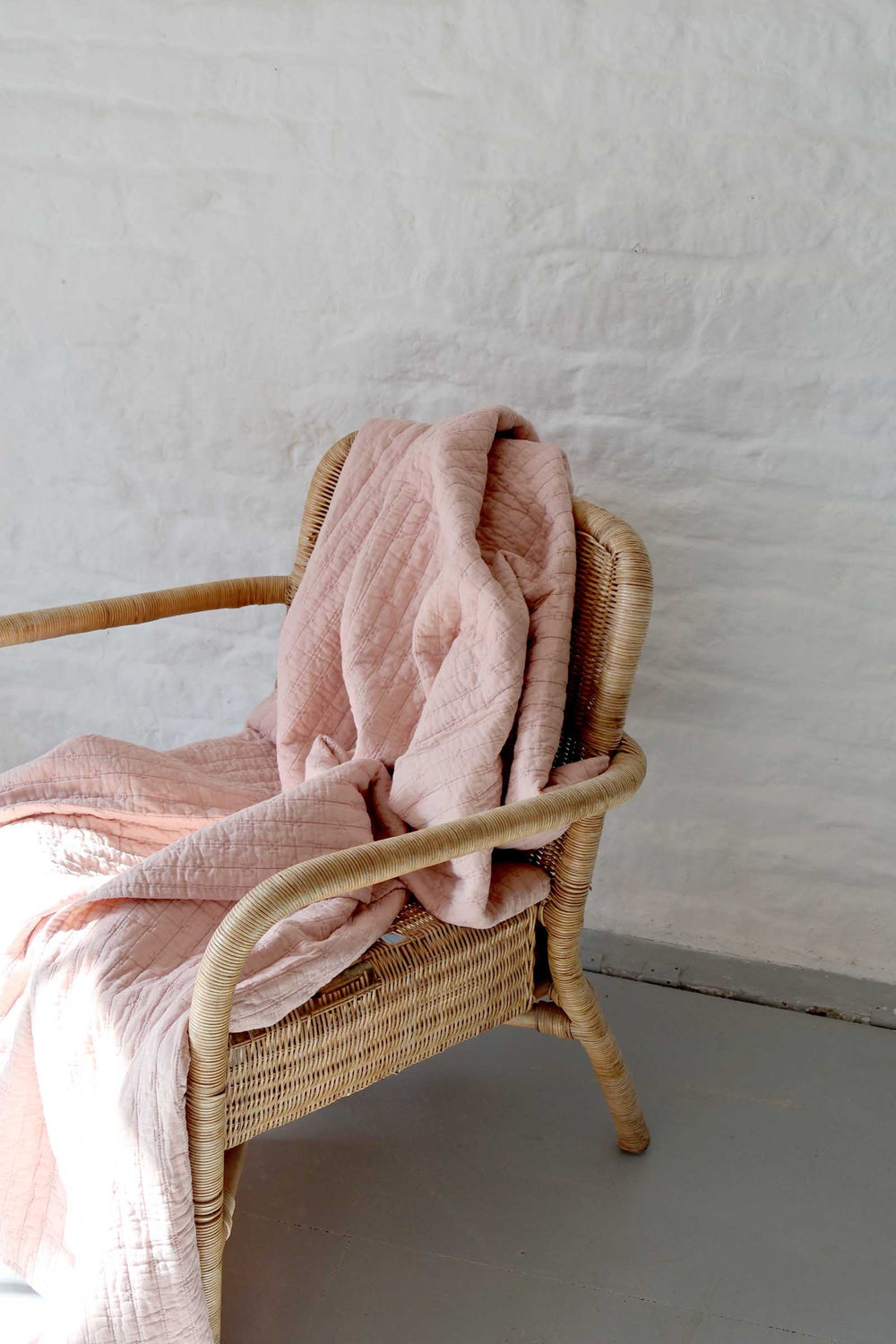 Wicker chair with a pink blanket against a plain wall.