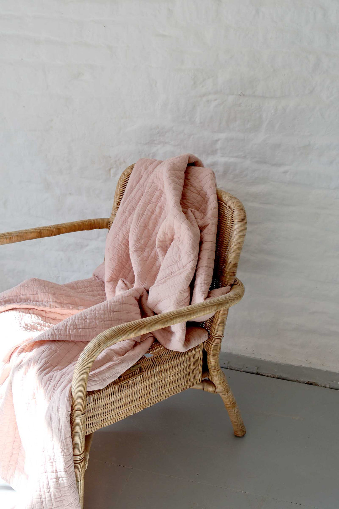 Wicker chair with a pink blanket against a plain wall.