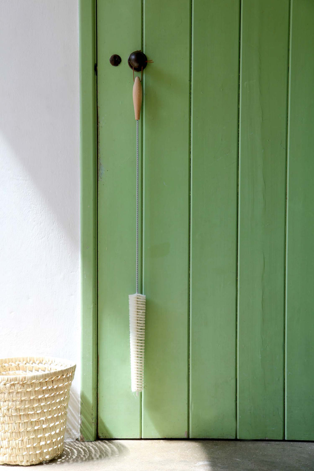 Green wooden cabinet with a brush hanging on it, next to a woven basket.
