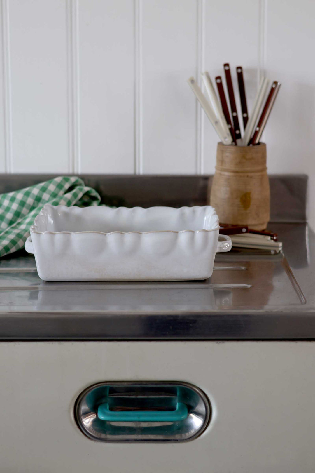 White ceramic dish on a metal surface with a wooden container of utensils in the background.