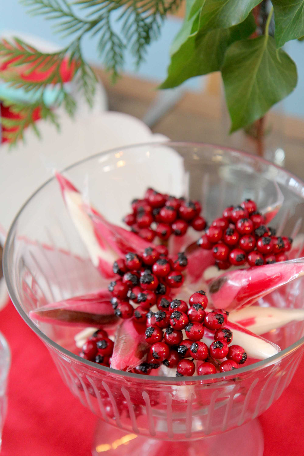 Clear glass bowl with red berries and pink flowers on a red surface