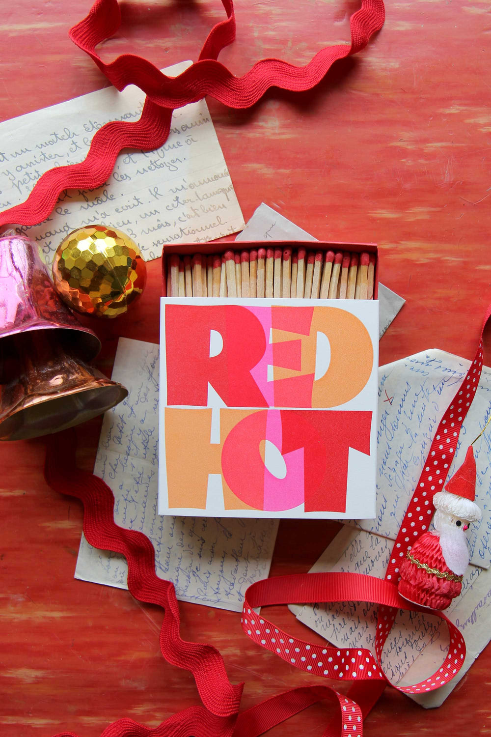 Matchbox with 'RED EYE' design on a red surface with decorative ribbons and confetti.