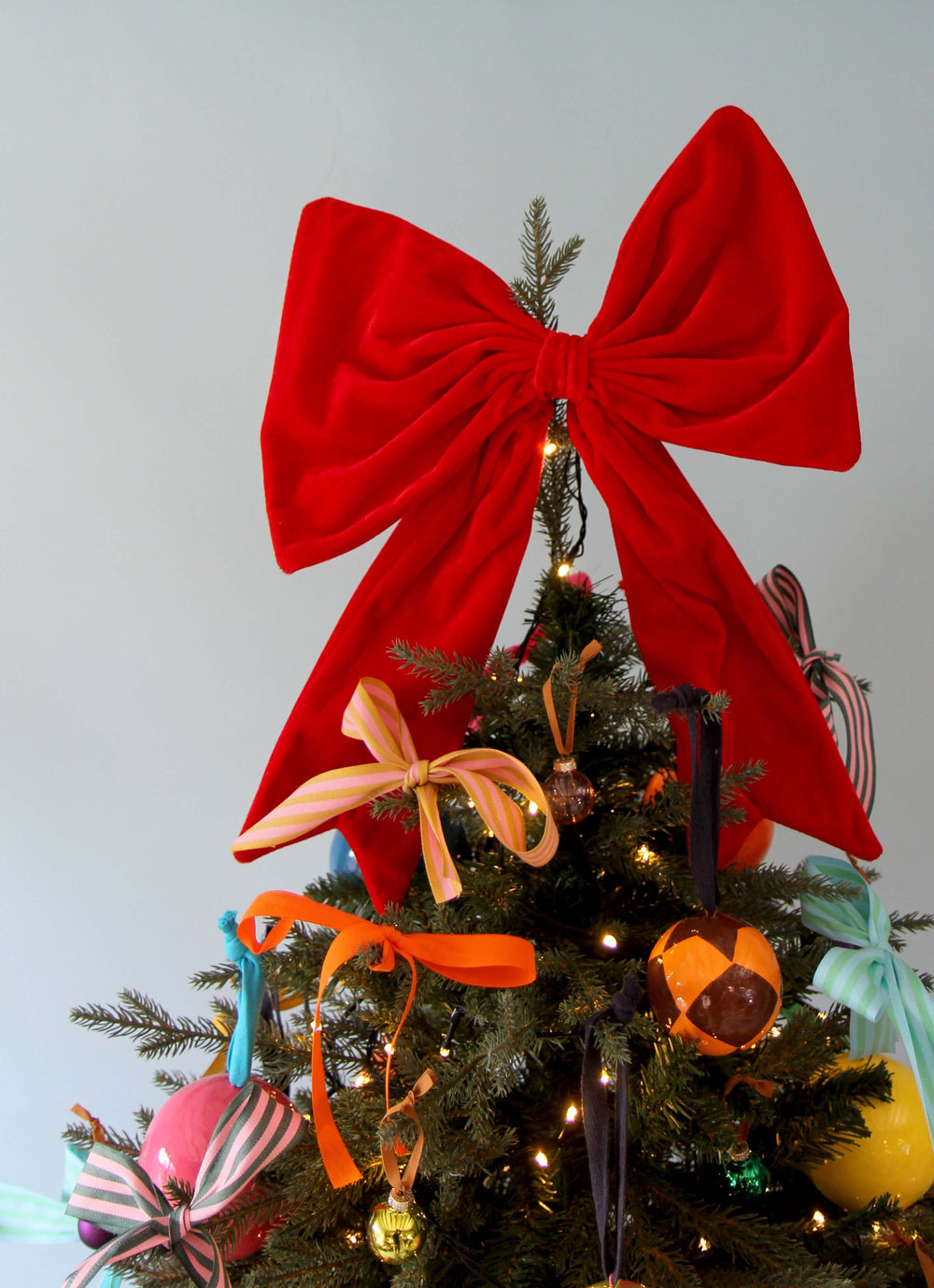 Decorated Christmas tree with a large red bow on top against a light blue background