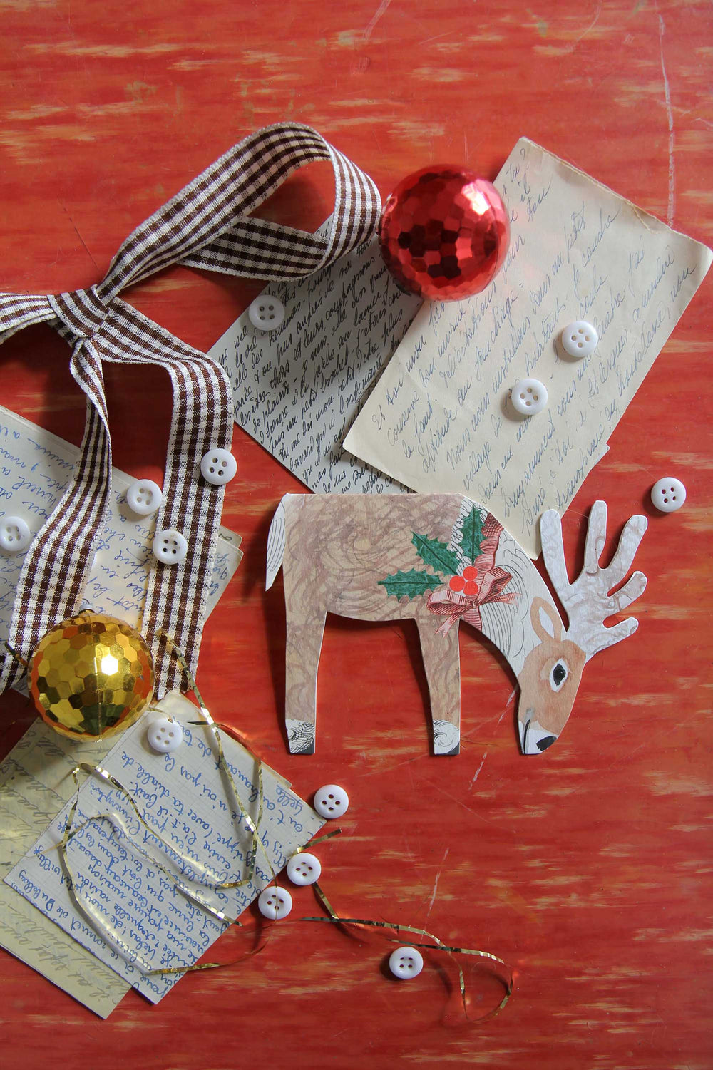 Decorative paper reindeer with buttons, ribbons, and ornaments on a red surface