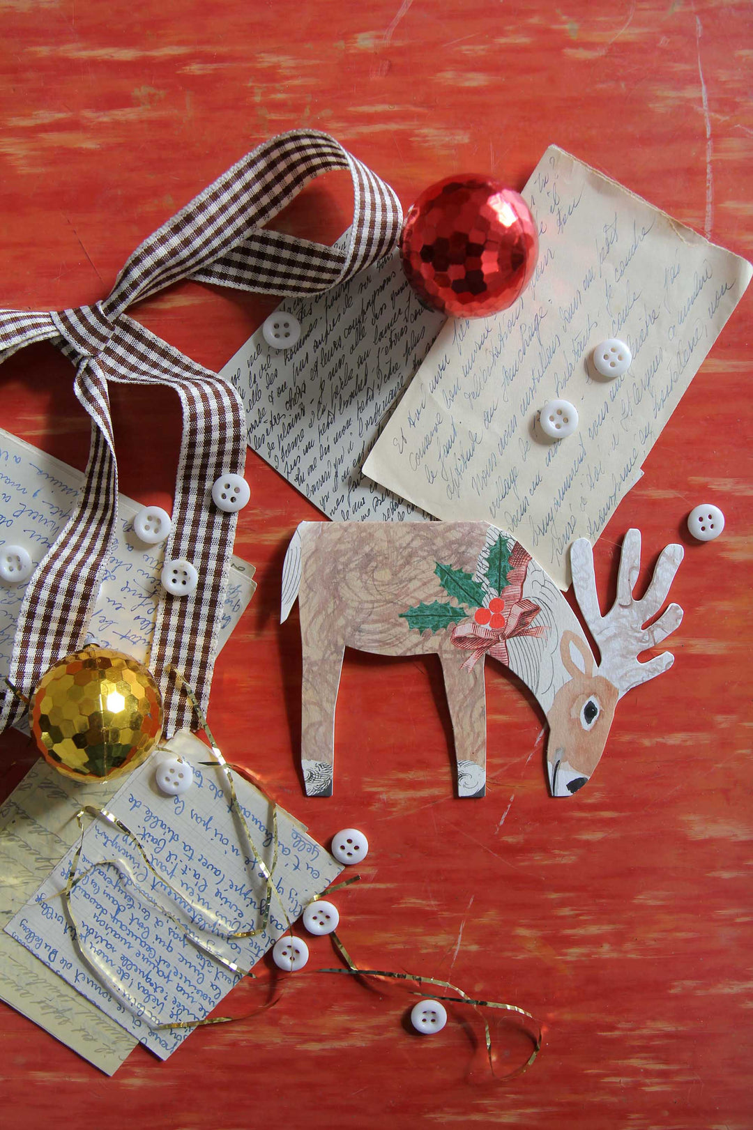 Decorative paper reindeer with buttons, ribbons, and ornaments on a red surface