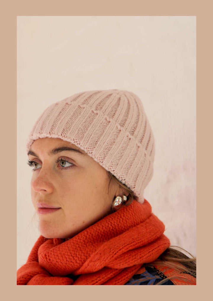 Woman wearing a pink knitted beanie and red scarf against a beige background