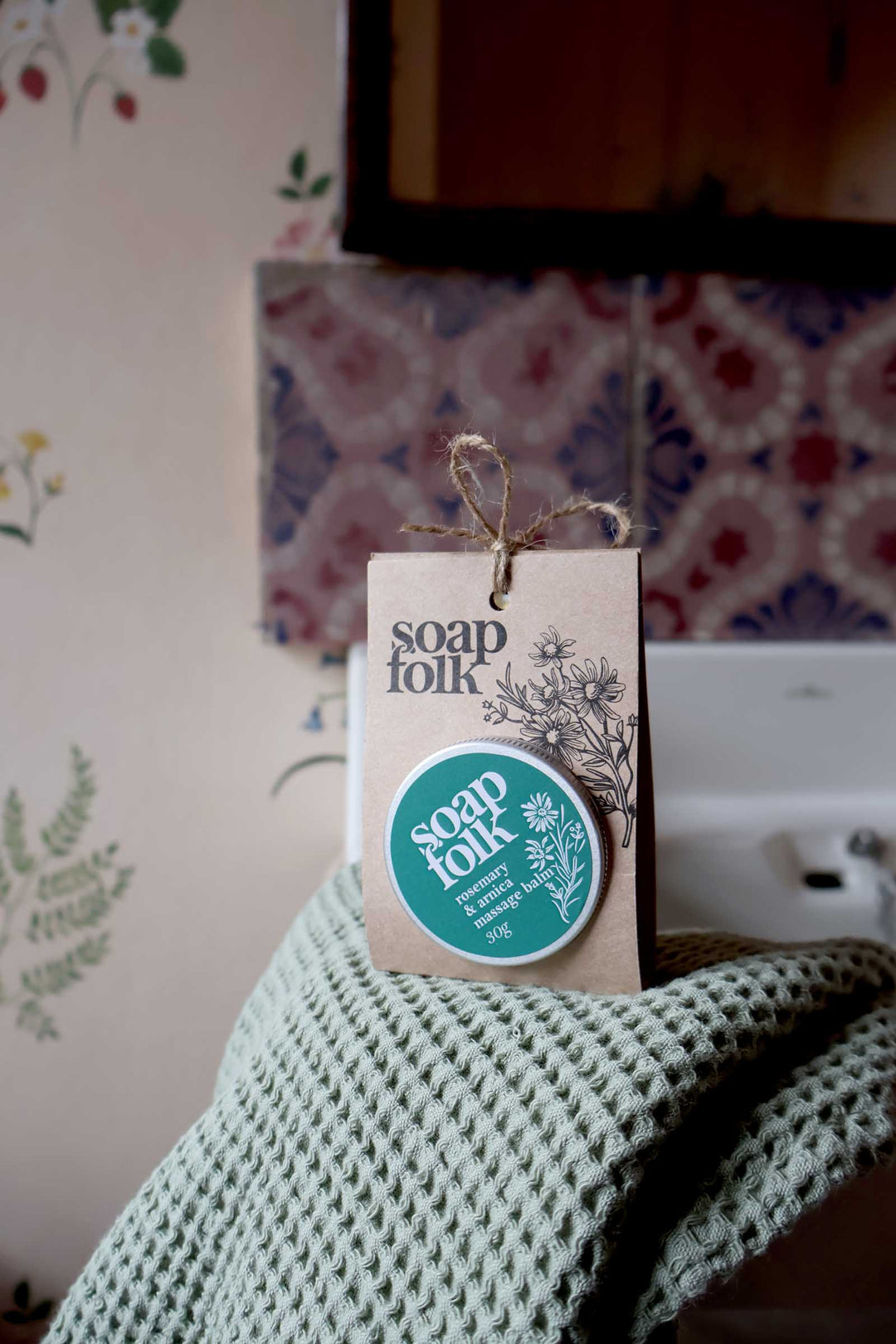 Soap Folk product packaging on a textured surface with a floral-patterned wall in the background