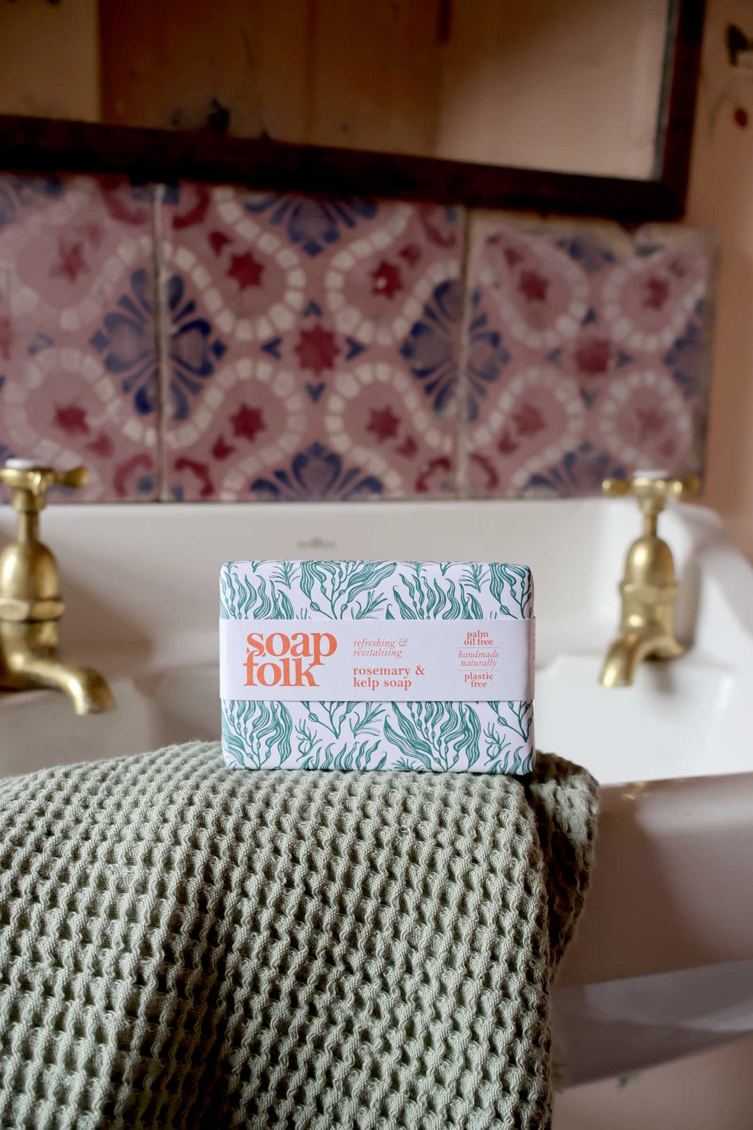 Bar of soap on a towel with a decorative tiled wall and sink in the background