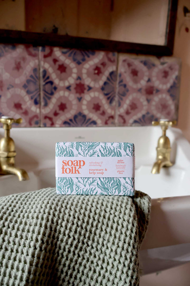 Bar of soap on a towel with a decorative tiled wall and sink in the background
