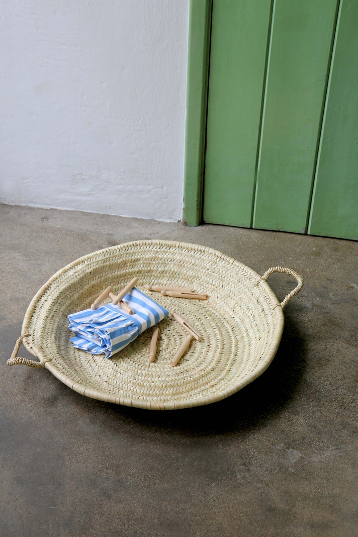 Woven basket with a blue and white striped towel on a concrete floor against a green wall.