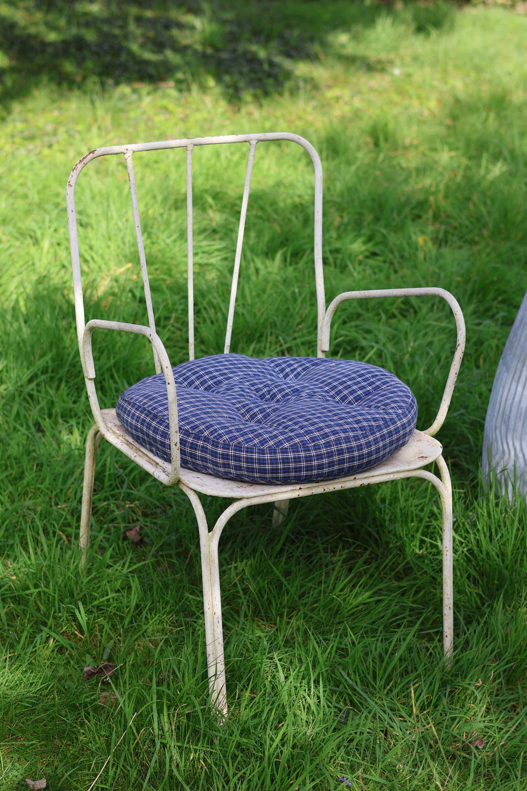 White metal chair with a blue cushion on a grassy background