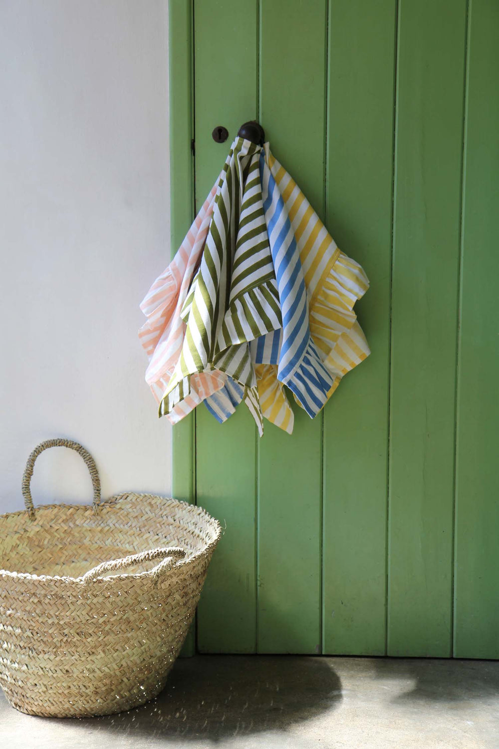 Colorful striped towels hanging on a hook against a green wall with a woven basket on the floor.