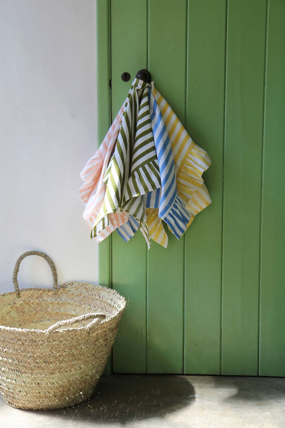 Colorful striped towels hanging on a hook against a green wall with a woven basket on the floor.