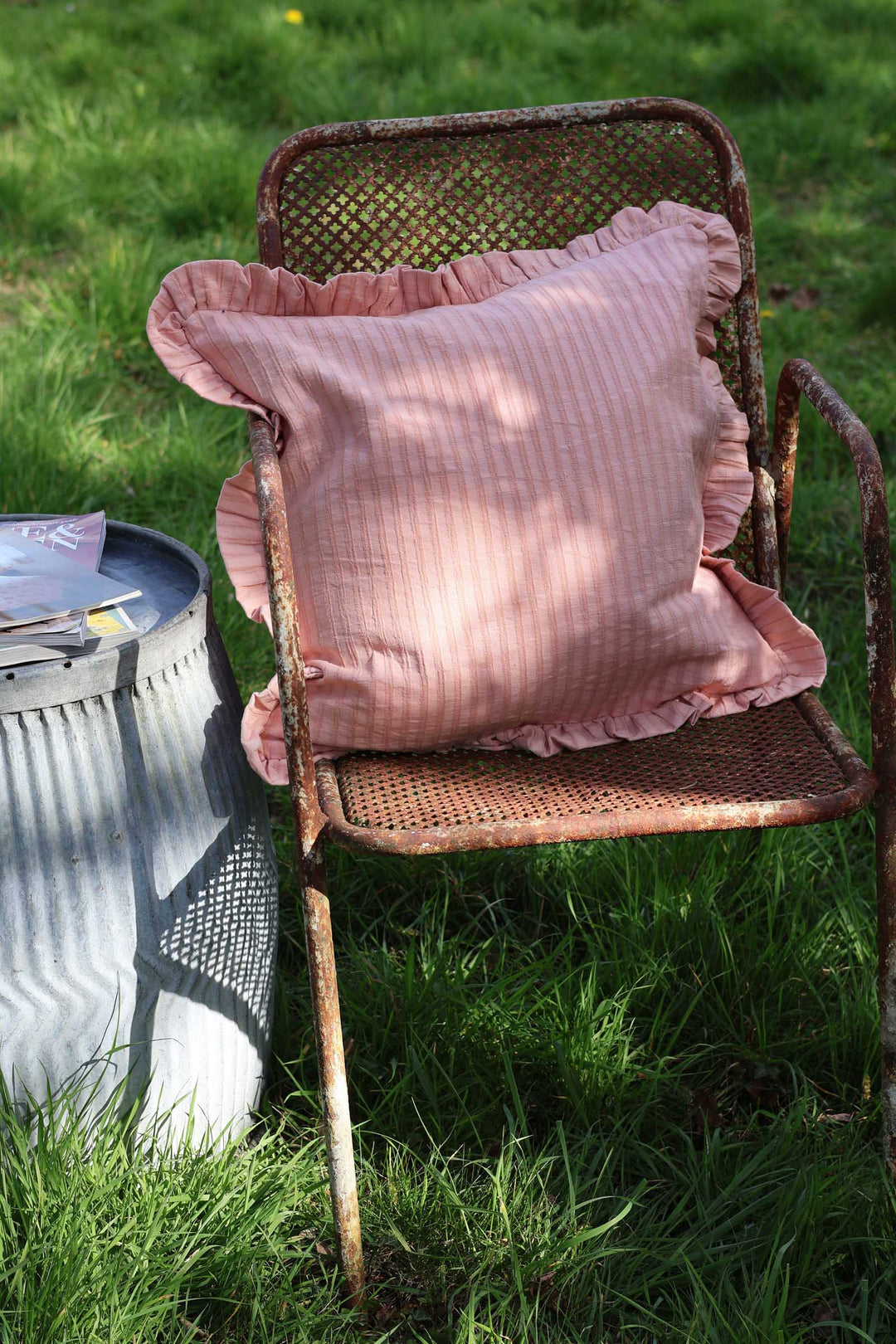 Pink cushion on a wicker chair in a grassy outdoor setting