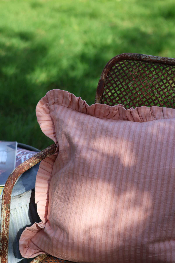 Pink striped pillow on a chair with a blurred green background