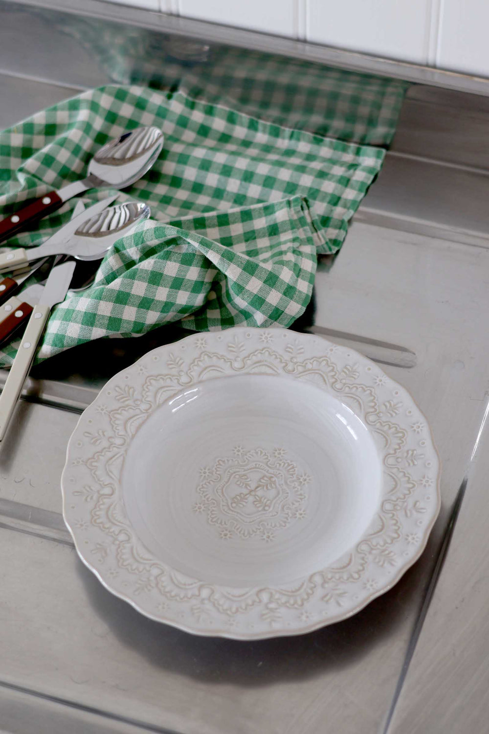 Decorative white plate with intricate patterns on a kitchen counter with green checkered towel and utensils.