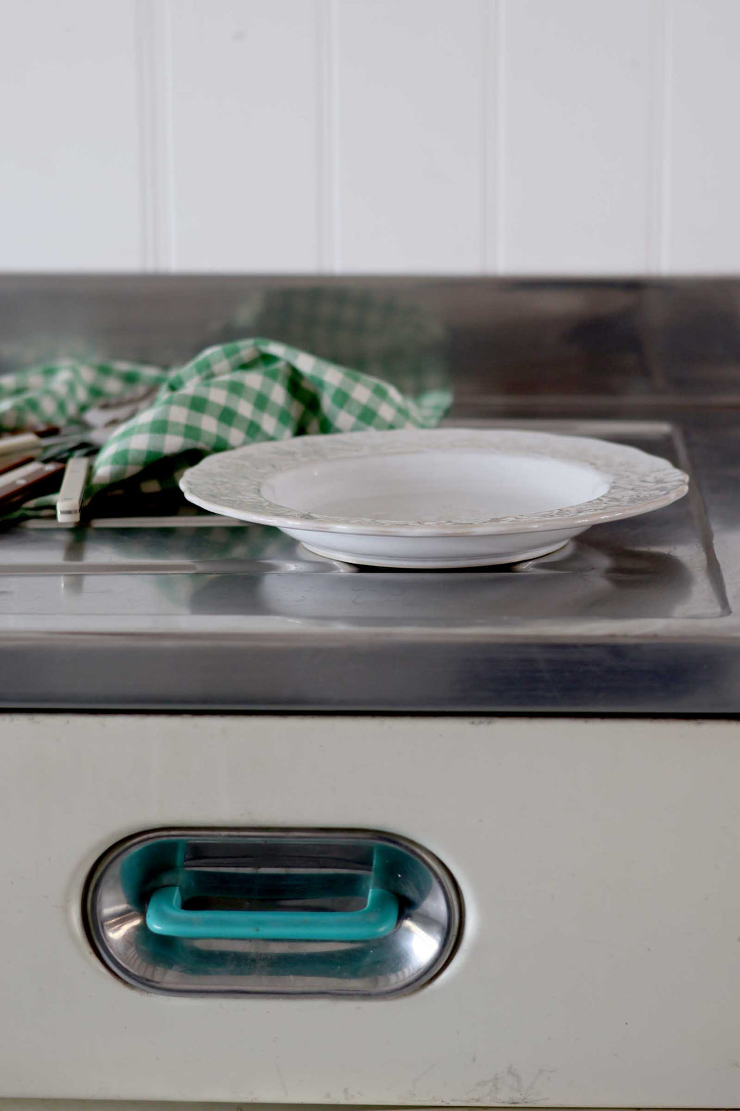 Stainless steel appliance with a white plate on top and a green checkered towel in the background.