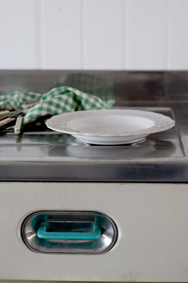 Stainless steel appliance with a white plate on top and a green checkered towel in the background.