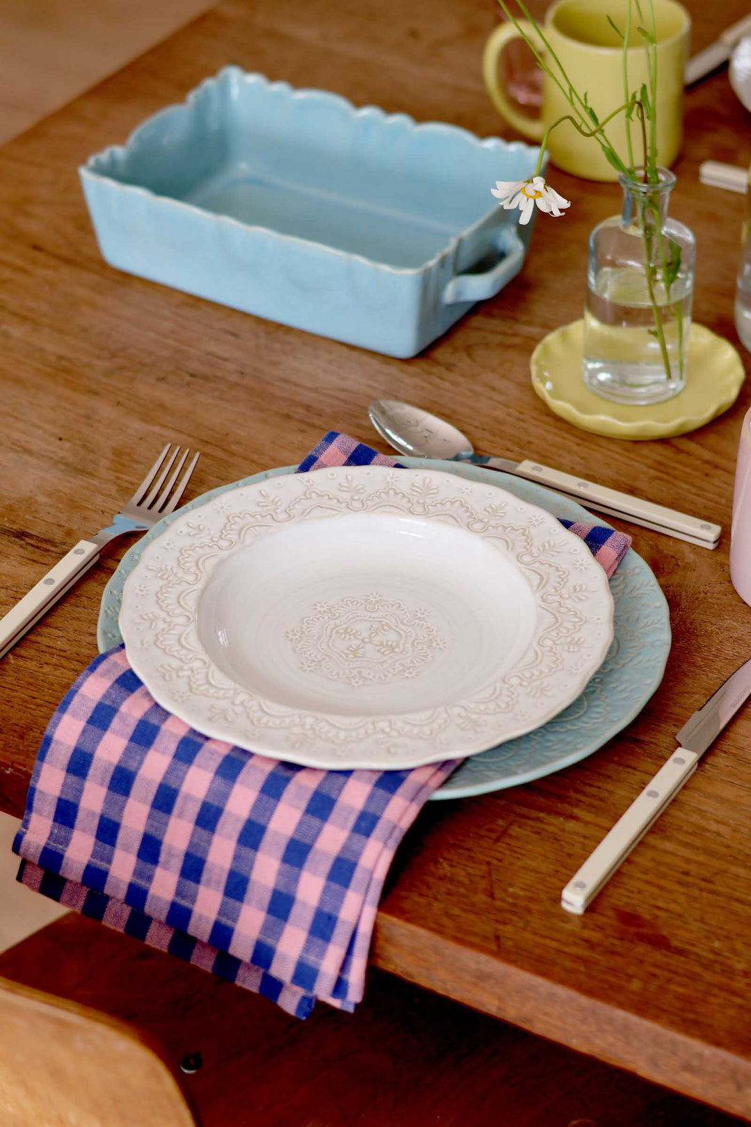Dining table setting with a white plate, blue platter, and checkered napkin.