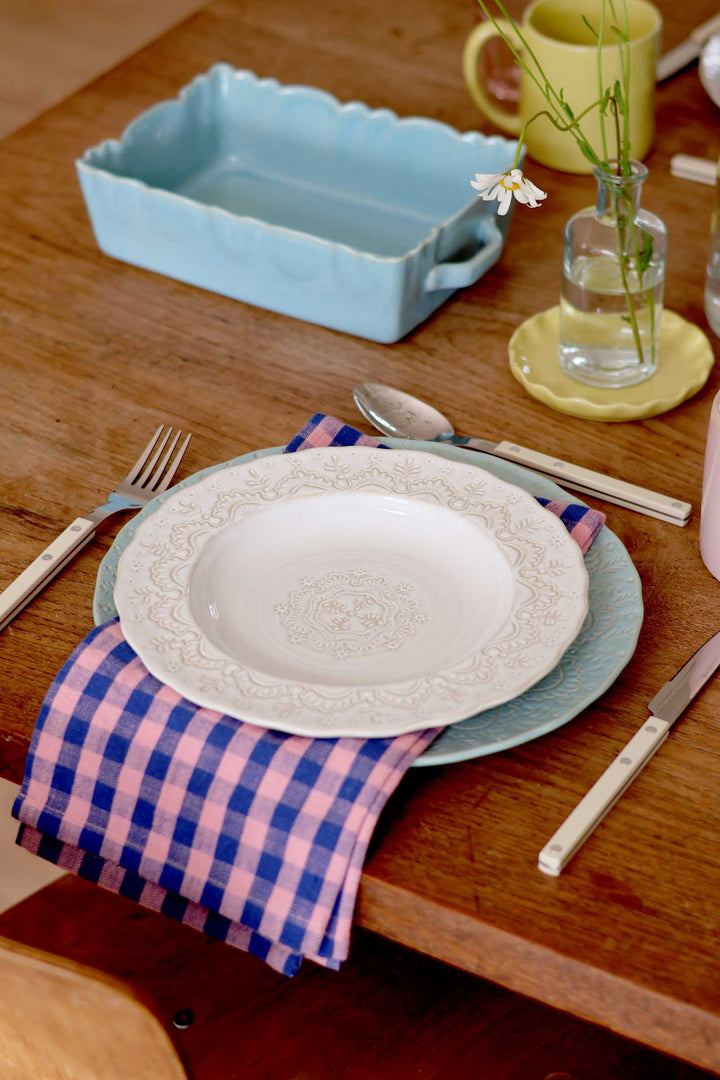 Dining table setting with a white plate, blue platter, and checkered napkin.