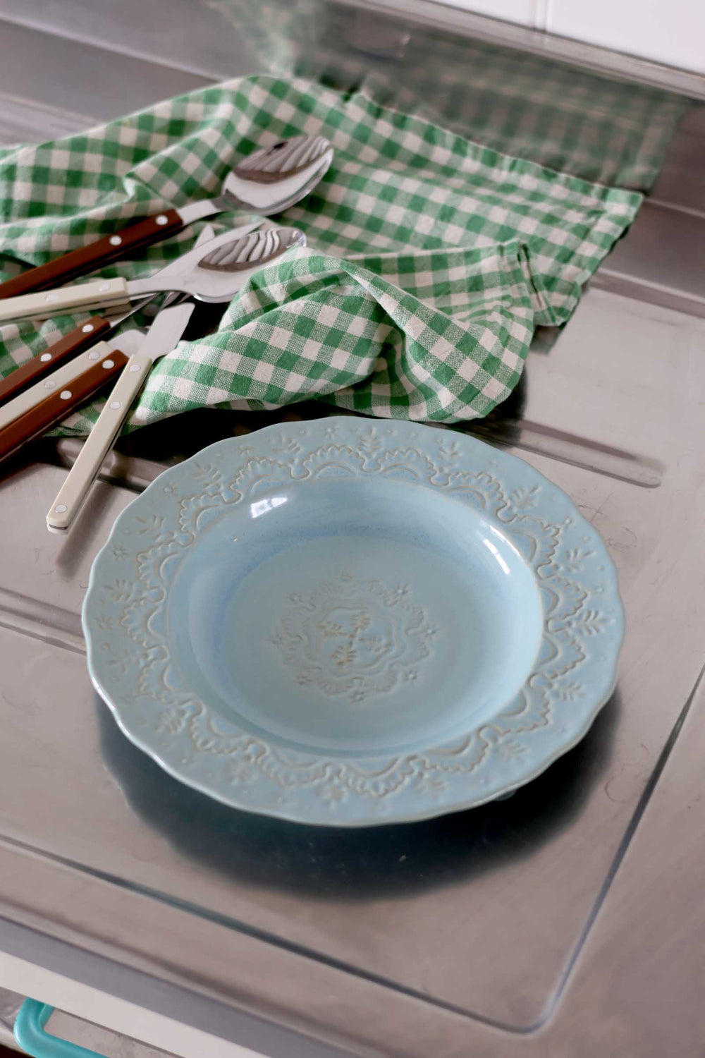 Blue ceramic plate with floral patterns on a metallic surface with green checkered cloth and utensils.