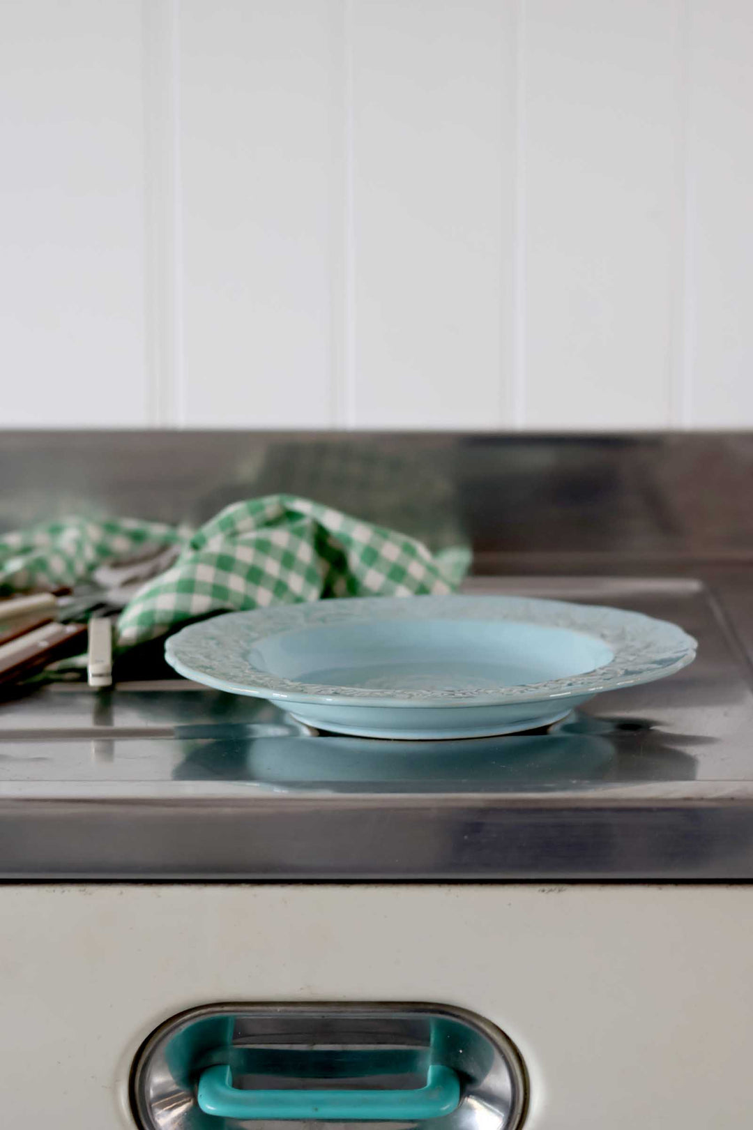 Teal plate on a stove with a checkered towel in a kitchen setting