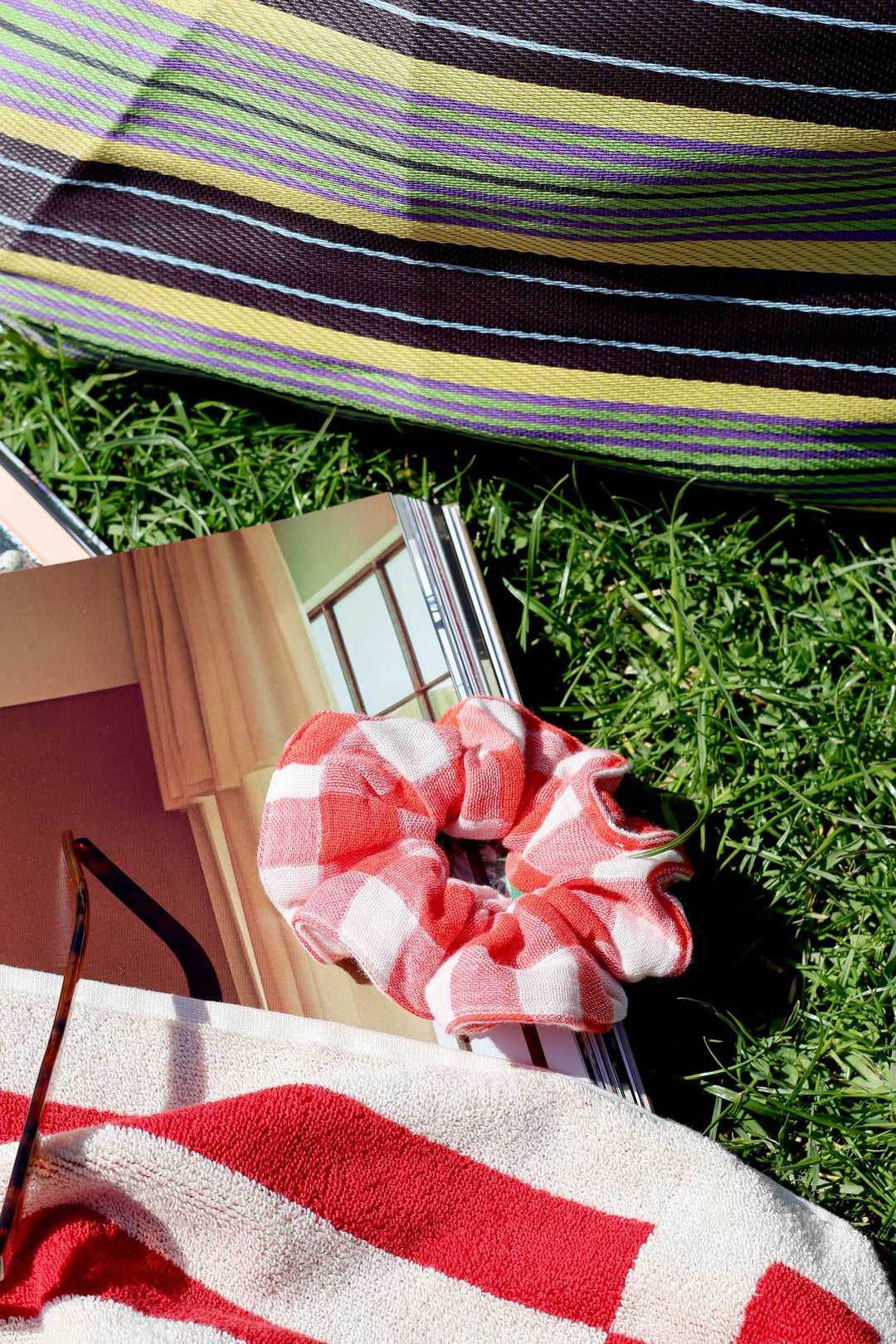 Pink checkered scrunchie on a grassy surface with a striped fabric in the background